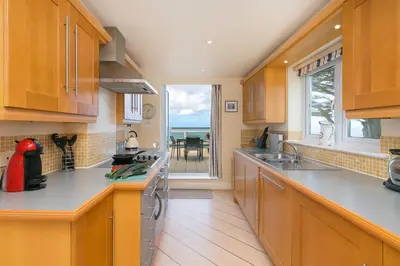 a kitchen with wooden cabinets and a view of the ocean at Ocean Gem in Carbis Bay