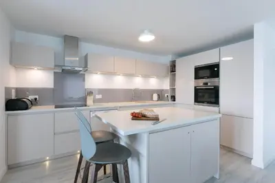 a kitchen with white cabinets and a blue chair at Golden Heights in Carbis Bay