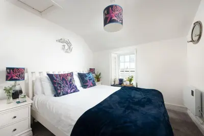 a bedroom with a large bed with blue and purple pillows at Mariners Cottage, St Ives in St Ives