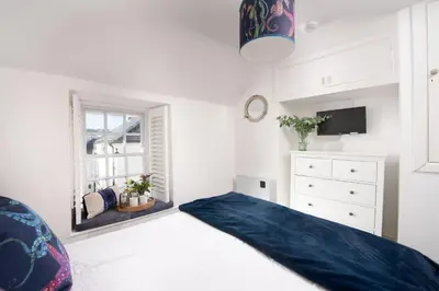 a white bedroom with a bed and a window at Mariners Cottage, St Ives in St Ives