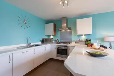 a kitchen with white cabinets and a blue wall at Sowena in Carbis Bay