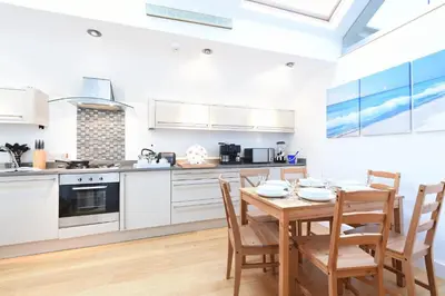 a kitchen with white cabinets and a wooden table and chairs at The Sail Loft in St Ives