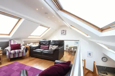 a living room with a black leather couch and a table at The Sail Loft in St Ives