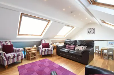 a living room with a leather couch and two chairs at The Sail Loft in St Ives