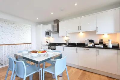 a kitchen with white cabinets and a table and chairs at Halcyon Cove in Carbis Bay