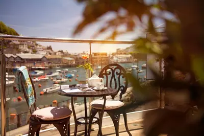 a table and chairs on a balcony with a view of a harbor at The Old Bridge House in Looe