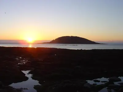 a sunset over a small island in the ocean at The Old Bridge House in Looe
