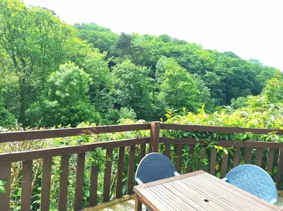 a wooden table and chairs on a deck with trees at Gorgeous Cottage at Crackington Haven, near Bude and Boscastle, Cornwall in Bude