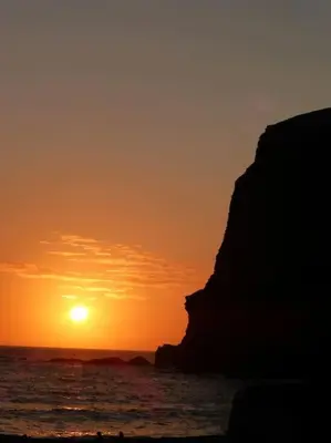 a sunset over the ocean with a rock in the foreground at Bantry Cottage at Crackington Haven, near Bude and Boscastle, Cornwall in Bude