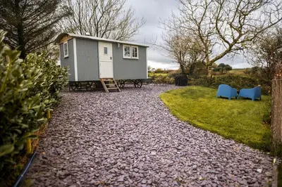 a tiny house in a yard with two blue chairs at Luxury Shepherd's Hut on Meadow with Outdoor Bath in Mid Cornwall in Truro