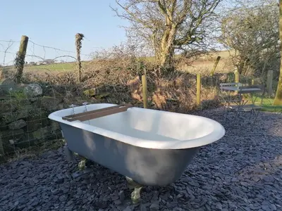 a bath tub sitting on the ground next to a fence at Luxury Shepherd's Hut on Meadow with Outdoor Bath in Mid Cornwall in Truro