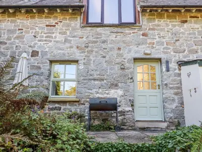 a stone house with a green door and a chair at The Mews in Bodmin