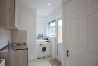 a white kitchen with a washing machine and a window at Anneth Lowen in Polzeath