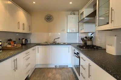 a kitchen with white cabinets and black counter tops at White Lodge - Coast Hideaways in Mawgan Porth