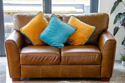 a brown leather couch with three pillows on it at Cancleave - Cornish Clifftop Luxury in Bude