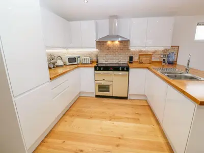 a kitchen with white cabinets and a wooden floor at 12 Faraway Fields in Liskeard