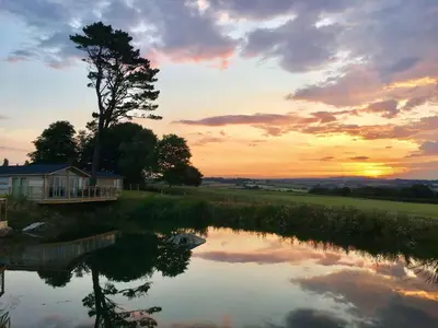 a sunset over a pond with a tree and a house at 12 Faraway Fields in Liskeard