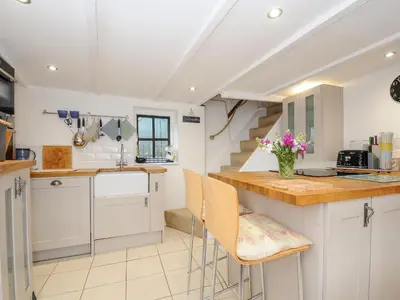 a kitchen with white cabinets and a counter with chairs at Church View Cottage in Looe