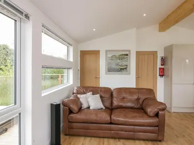 a brown leather couch in a living room with windows at 7 Meadow Retreat in Liskeard