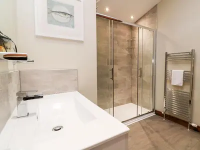 a white bathroom with a shower and a sink at 2 Southern Place in Liskeard