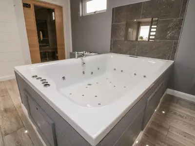 a large white tub in a bathroom with a mirror at 19 Meadow Retreat in Liskeard