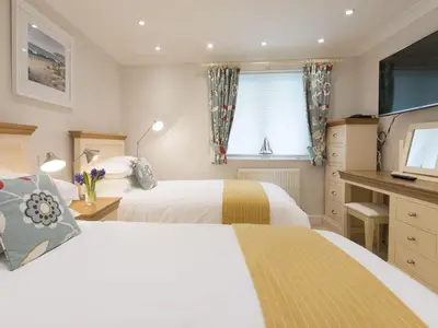 a bedroom with two beds and a desk and a television at Surf and Sand in St Ives