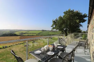 a table and chairs on a balcony with a view at Pol Glas Hall in Helston