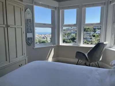 a bedroom with a chair in front of windows at Mevagissey Holiday Home - sea view and parking in St Austell