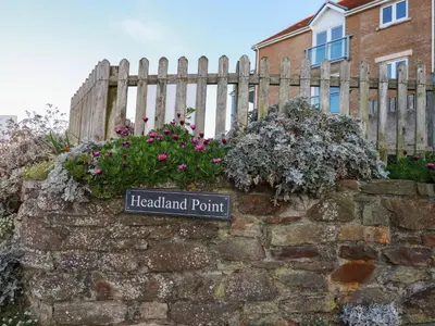 a sign on a stone wall with flowers at 9 Headland Point in Newquay