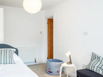 a white bedroom with a bed and a chair at Obo's Retreat in Wadebridge