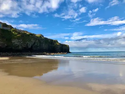 a sandy beach with the ocean and a cliff at WildView Cosy Glamping with Outdoor Bath and stunning scenery in Helston