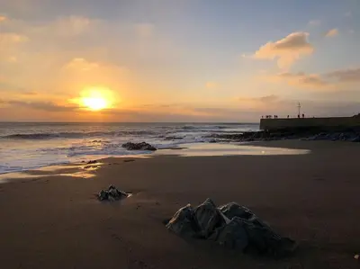 a sunset on the beach with a rock in the sand at WildView Cosy Glamping with Outdoor Bath and stunning scenery in Helston