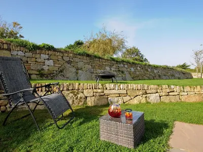 a yard with a stone wall and a table with a drink at Zephyr in Helston