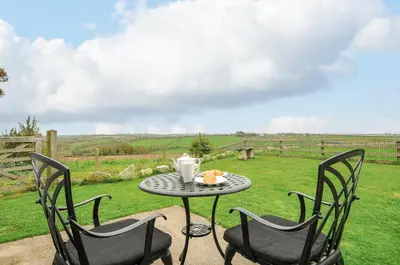 a table and chairs on a patio with a view of a field at Pol Glas Cabin in Helston