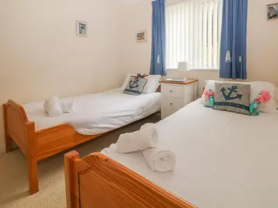 two beds in a room with blue curtains at Morton Cottage in Falmouth