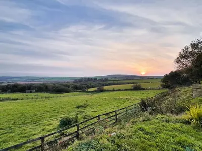 a fence in a field with the sunset in the background at Skyber Barn, a rural retreat on Bodmin Moor in Liskeard
