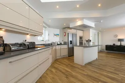 a large kitchen with white cabinets and wooden floors at Starboard in Carbis Bay