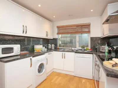a kitchen with white cabinets and a washer and dryer at Trebisken - Cottage in Porthtowan