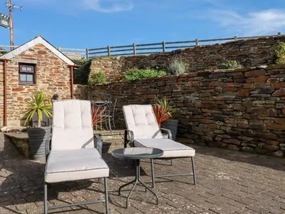 two chairs and a table in front of a stone wall at Great Meadow Barn in Newquay
