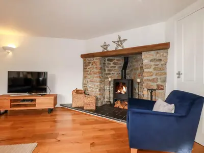 a living room with a fireplace and a blue chair at Great Meadow Barn in Newquay
