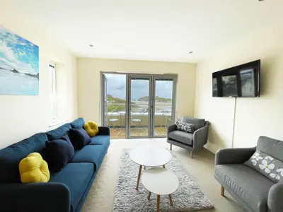a living room with a blue couch and two chairs at 5 The Beach House in Saint Columb Minor