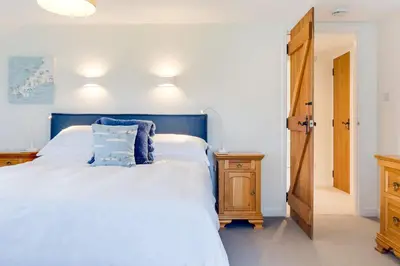 a bedroom with a large white bed with a blue headboard at Goose Cottage - within the Helland Barton Farm collection in Delabole