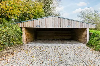 a brick garage with a roof on a gravel road at Courtyard Cottage - within the Helland Barton Farm collection in Delabole