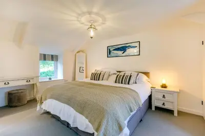 a white bedroom with a bed and a window at The Old Bakehouse - within the Helland Barton Farm collection in Delabole