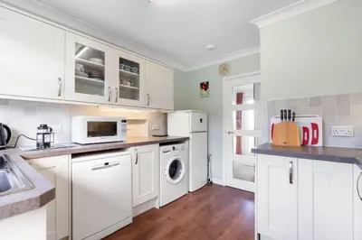 a kitchen with white cabinets and a washer and dryer at Gwel Teg, 30 Egerton Road in Padstow