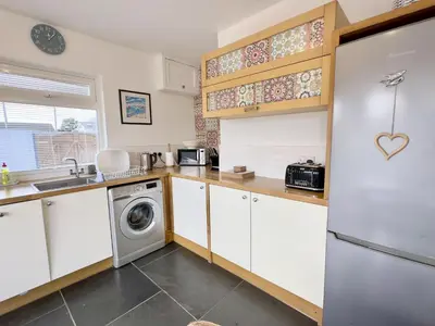 a kitchen with white cabinets and a washer and dryer at Hardown in St Merryn