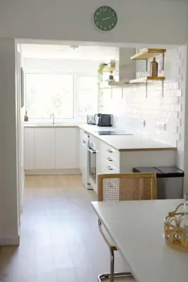 a kitchen with white cabinets and a clock on the wall at The Palm House Falmouth - minutes from the beach! in Falmouth