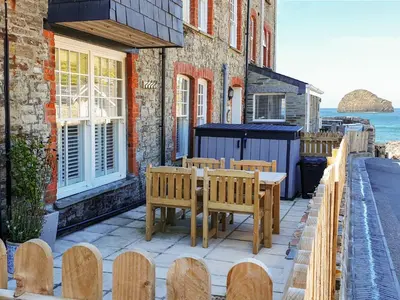 a patio with wooden benches and a table and chairs at Salty Sea Dog in Tintagel