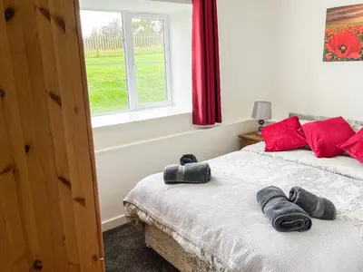 a bedroom with a bed with red pillows and a window at Four Burrows Bungalow in Chacewater
