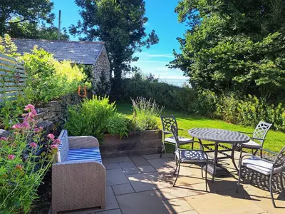 a patio with a table and chairs in a garden at Appleloft in Saint Gennys